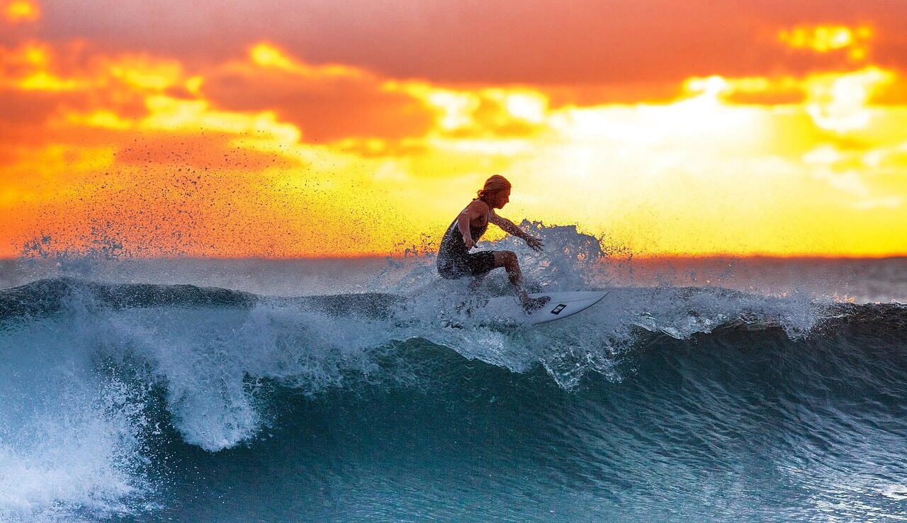 Surfer skillfully navigates a wave at sunset, showcasing dynamic action against a vibrant sky. Captures the thrill of surfing.