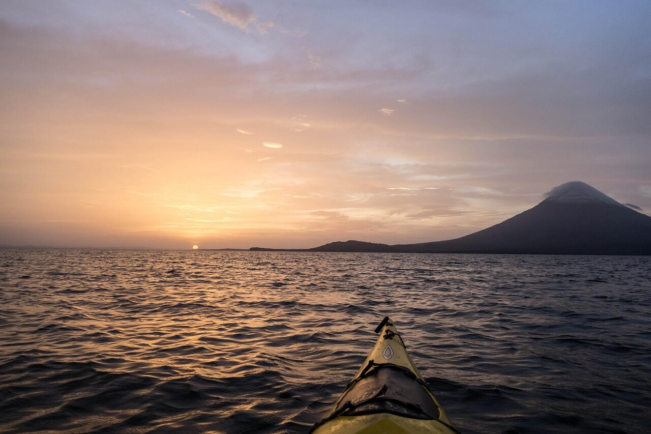Kayaking on calm waters at sunset, with a volcano silhouette in the background, capturing a serene moment in nature's beauty.