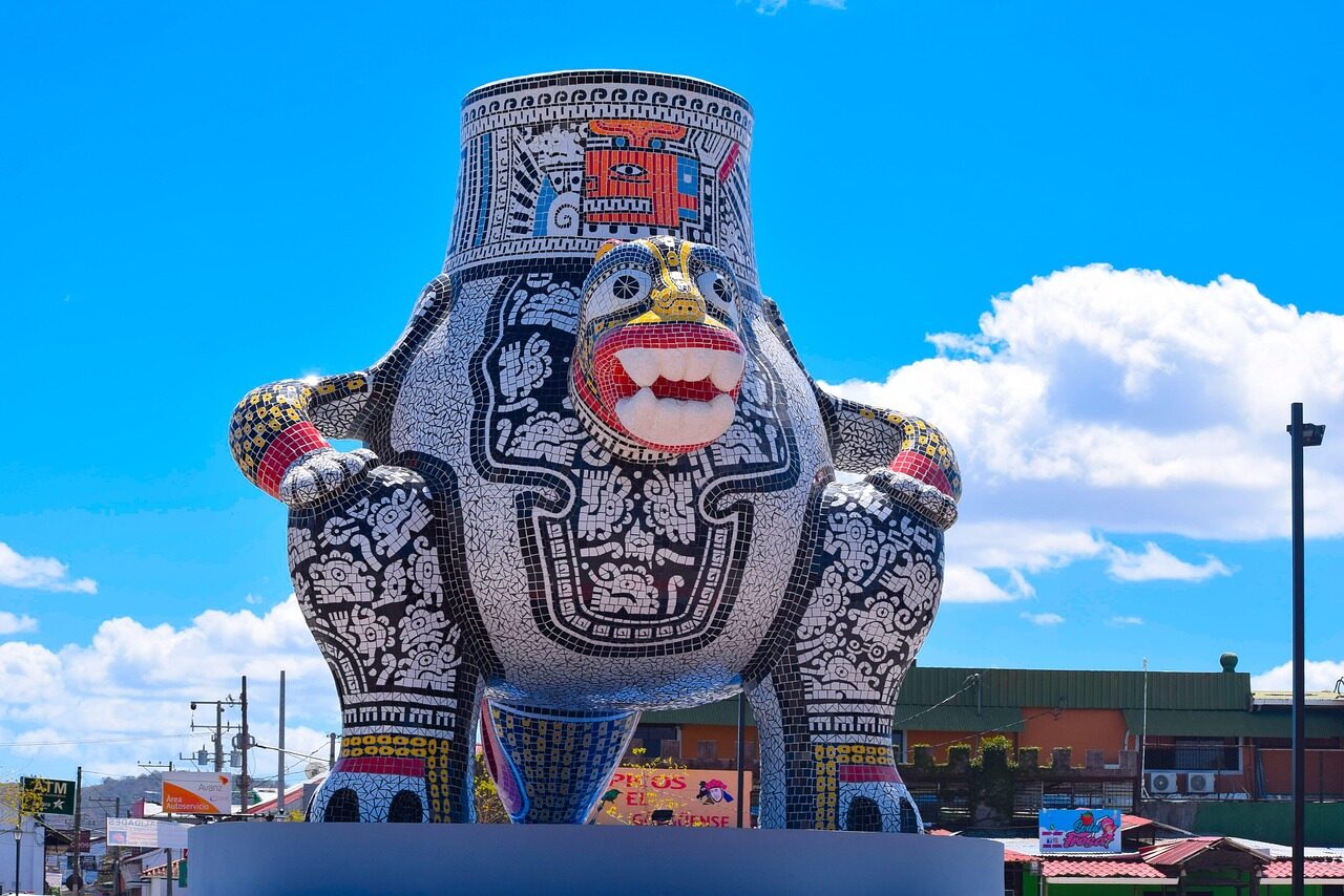 Colorful ceramic statue of a large smiling figure resembling traditional folklore, set against a bright blue sky. Represents local culture and art.