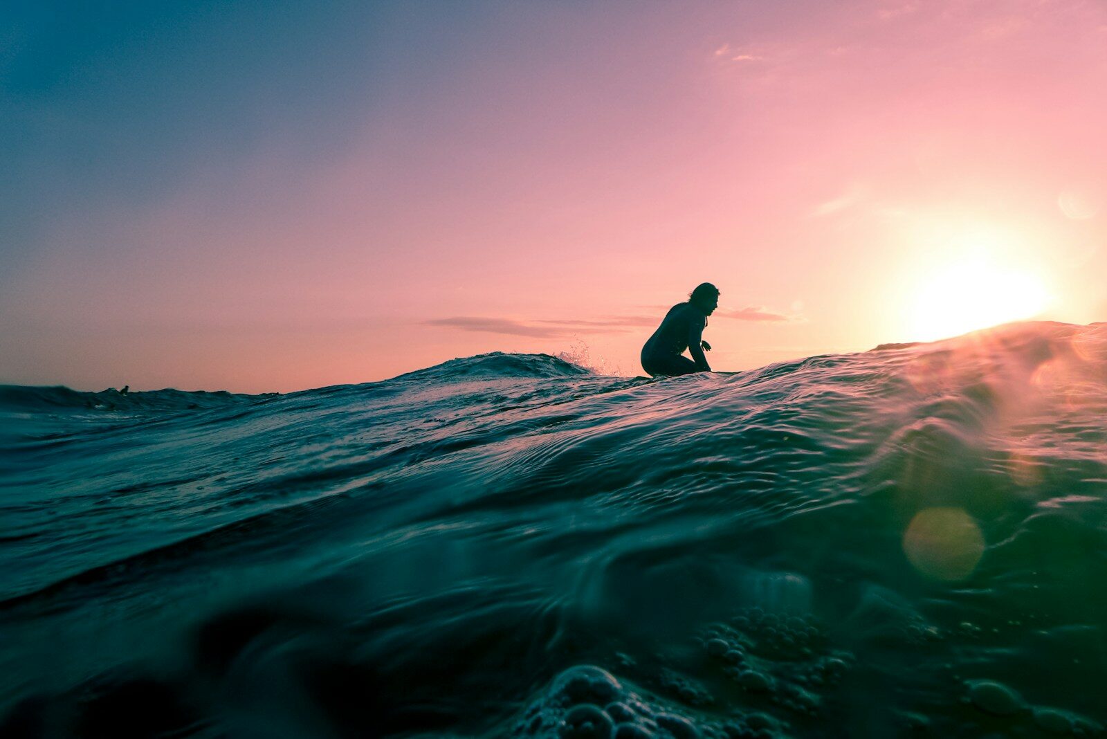 Surfer silhouetted against a vibrant sunset, catching a wave in an ocean setting, highlighting the sport’s dynamic nature and beauty.