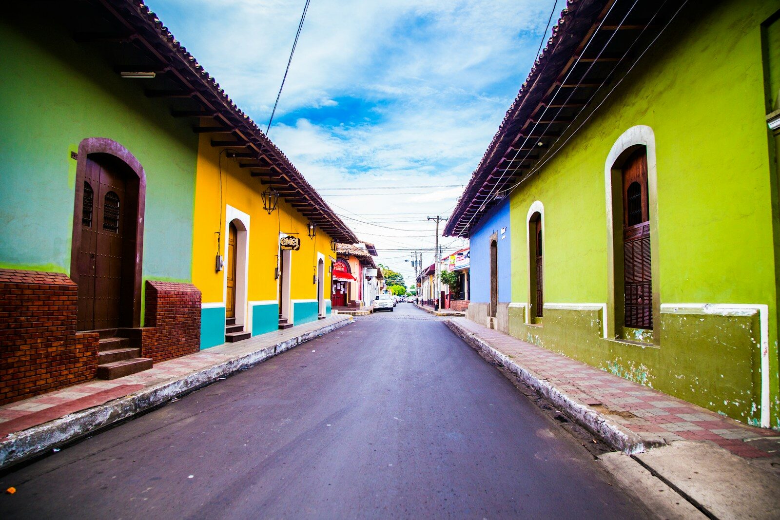 Colorful colonial buildings line a quiet street in a vibrant town, showcasing green, yellow, and blue facades under a bright sky.